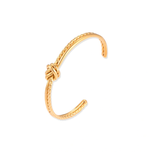 Gold cuff bracelet with twisted rope texture and decorative knot centerpiece on cream background.
