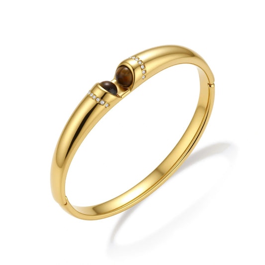 Polished gold bangle with two oval tiger's eye cabochons flanked by pavé diamond accents at center clasp.