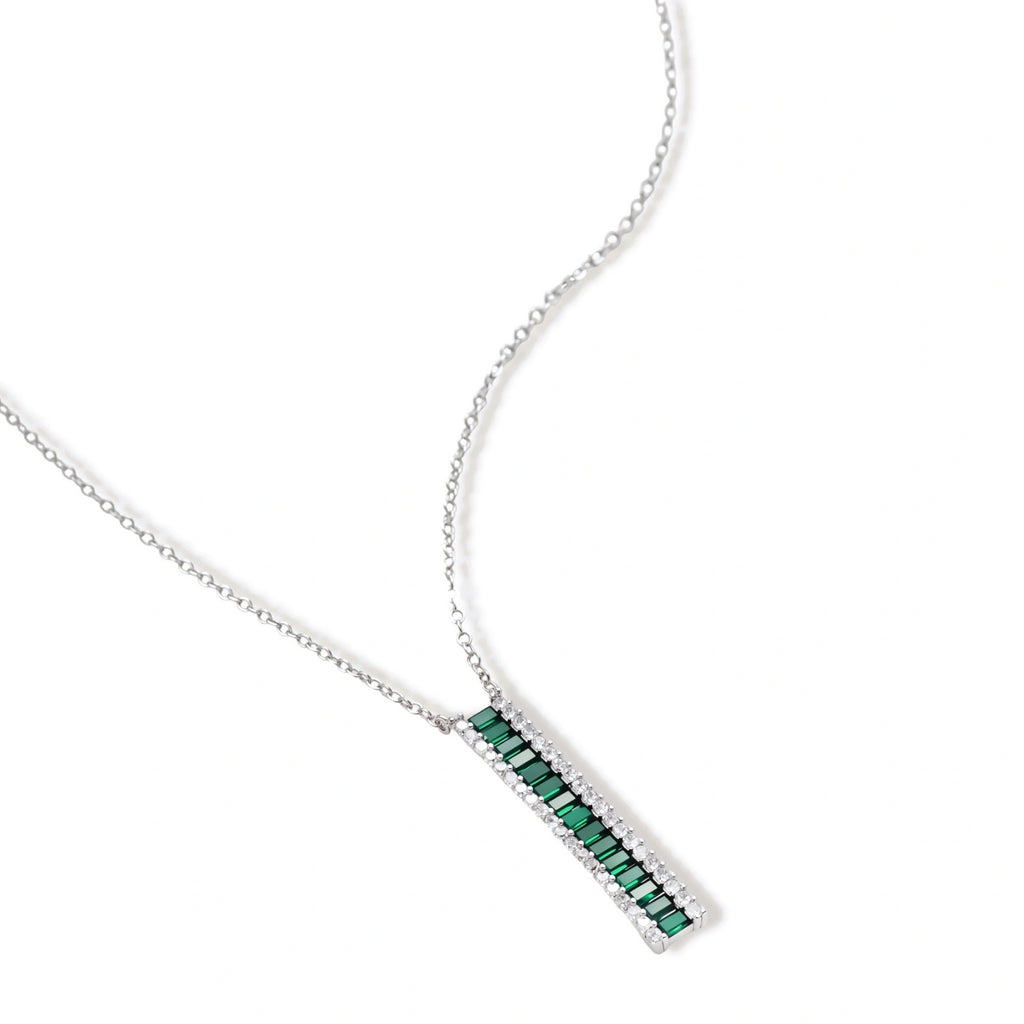White gold plated jewelry set with emerald green rectangular stones and clear crystals in geometric rows on white background.