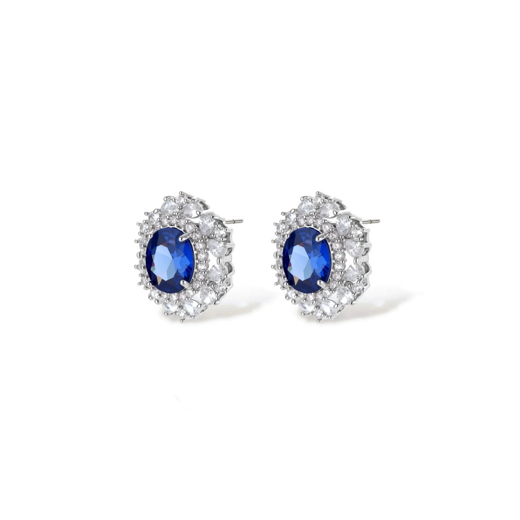 White gold plated jewelry set with blue cubic zirconia centers surrounded by clear crystal halos on cream background.