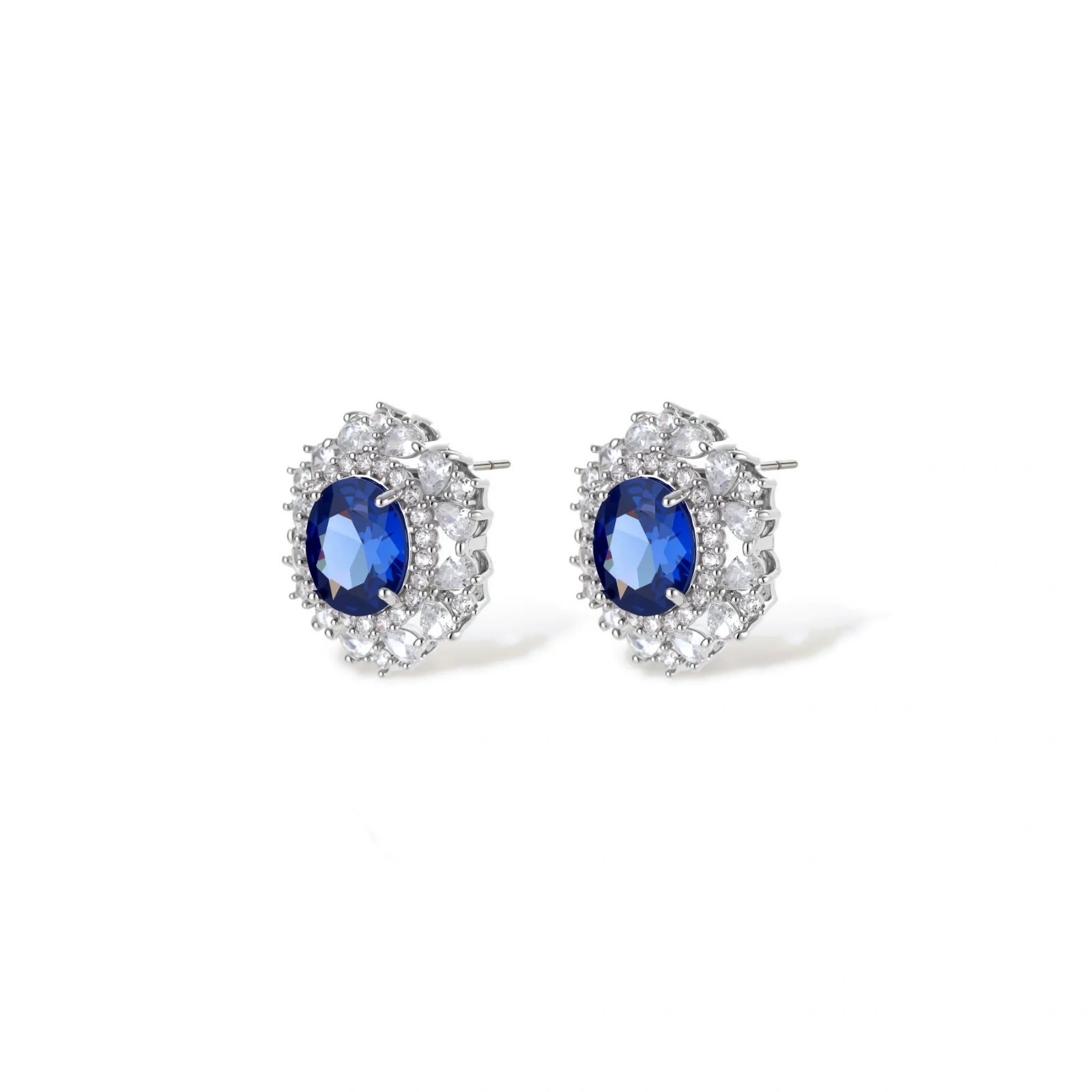 White gold plated jewelry set with blue cubic zirconia centers surrounded by clear crystal halos on cream background.