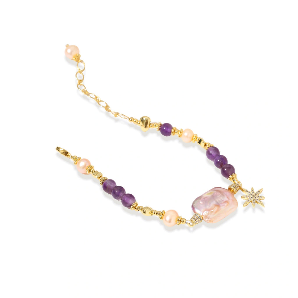 Gold-plated bracelet with baroque pearl centerpiece, amethyst beads, and crystal star charm on white background.