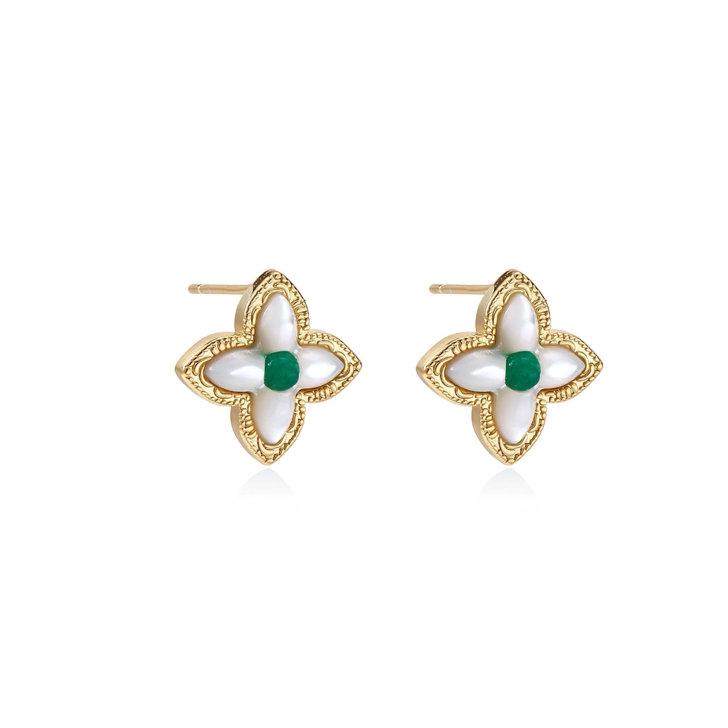 Gold quatrefoil stud earrings with white mother-of-pearl petals and emerald green gemstone center on beige background.