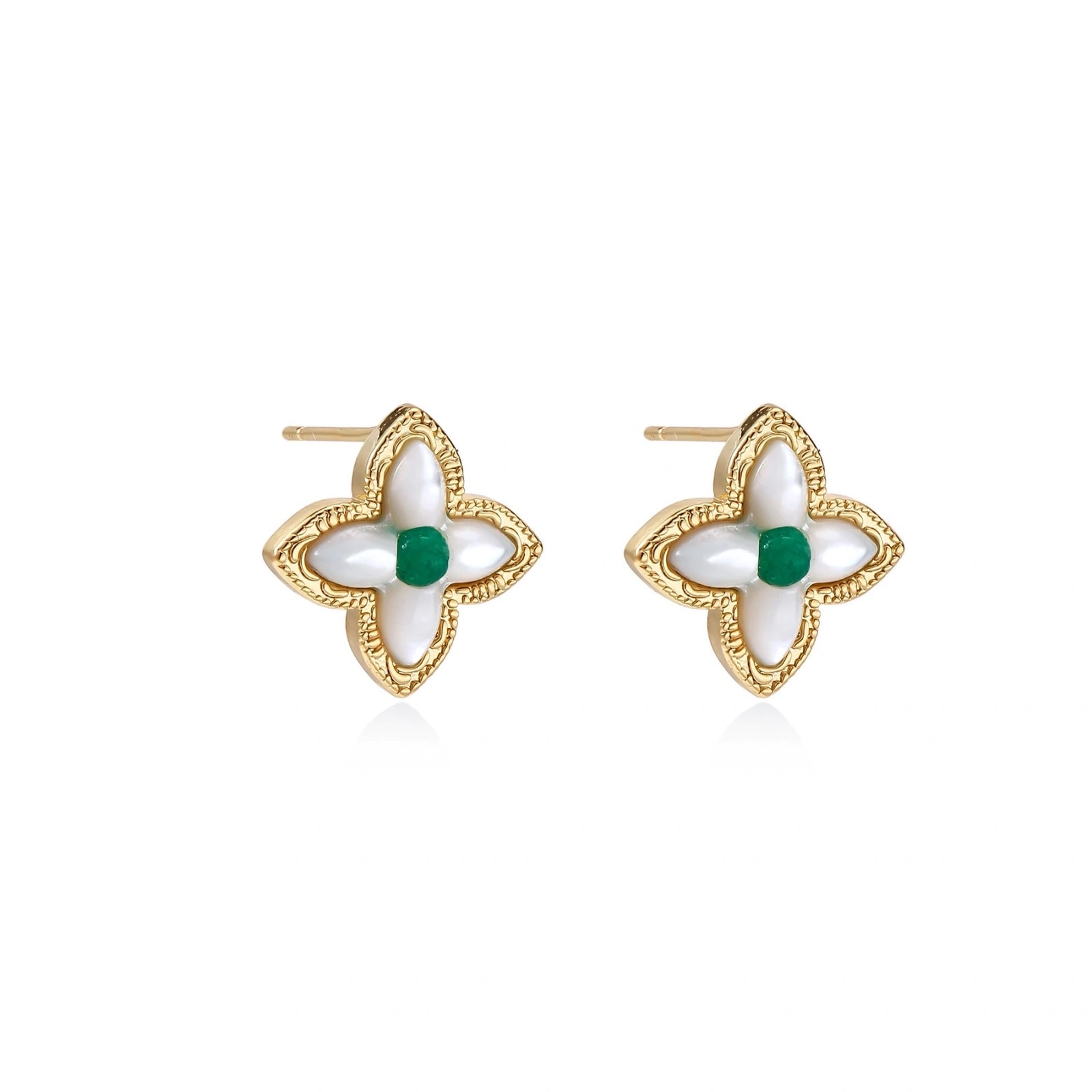 Gold quatrefoil stud earrings with white mother-of-pearl petals and emerald green gemstone center on beige background.