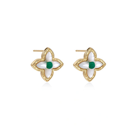 Gold quatrefoil stud earrings with white mother-of-pearl petals and emerald green gemstone center on beige background.