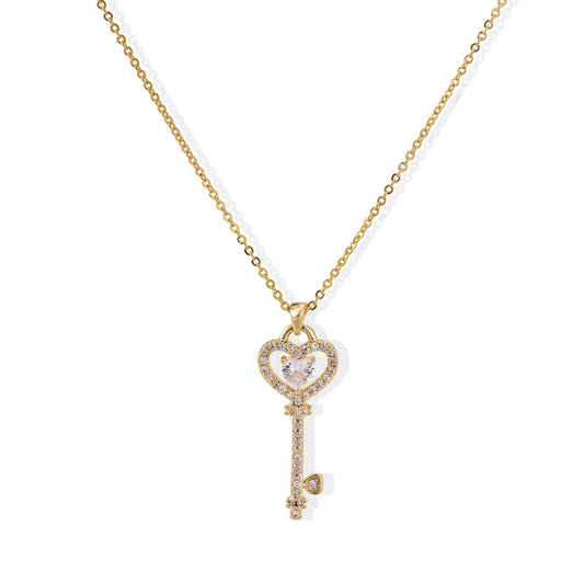 Delicate gold key pendant with heart-shaped bow and crystal pavé detailing on fine chain against cream background.