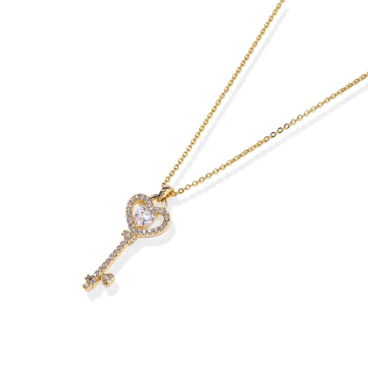 Delicate gold key pendant with heart-shaped bow and crystal pavé detailing on fine chain against cream background.