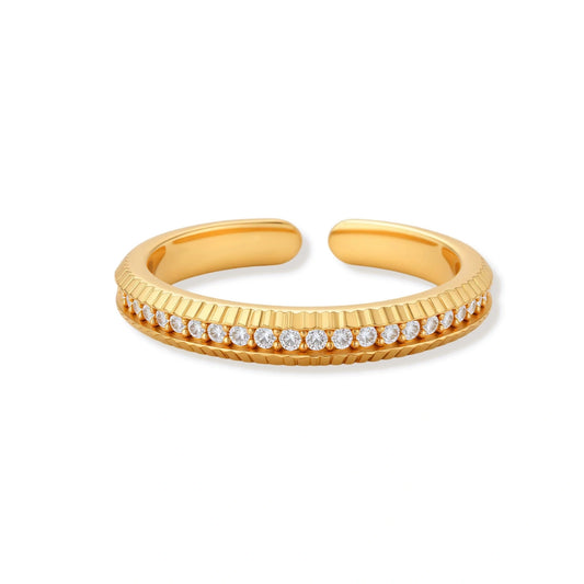 Adjustable gold-plated ring with row of sparkling crystals on ribbed band, shot against cream background