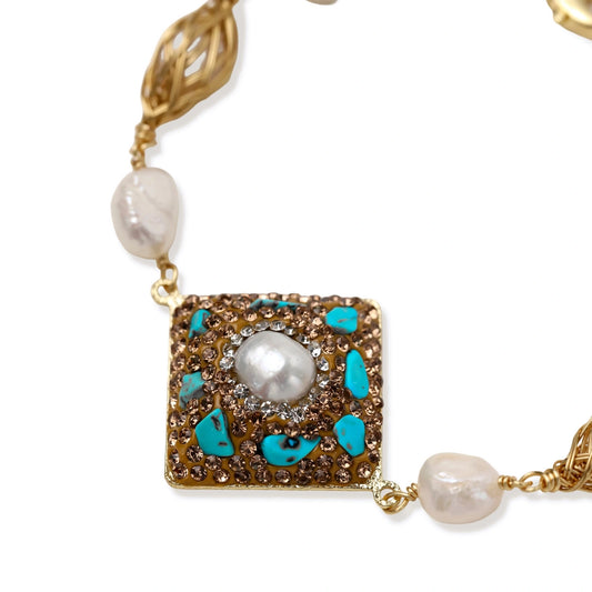 Gold-plated bracelet with baroque centerpiece, turquoise stones, freshwater pearls, and ornate chain links on cream background.