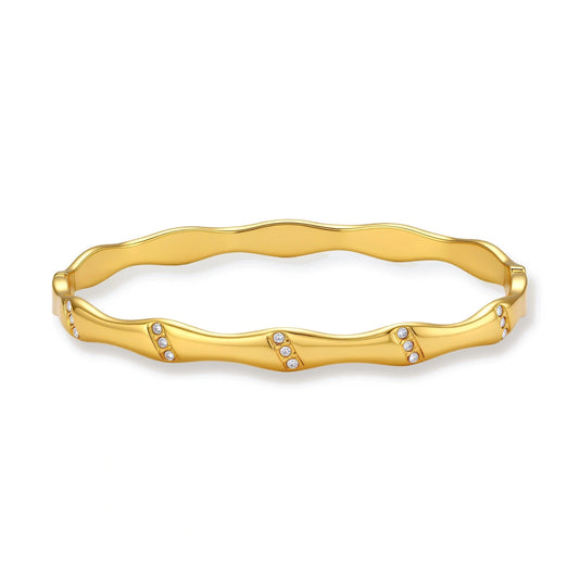 Gold-toned wavy bangle with bamboo-style segments and CZ crystal clusters on cream background. 18K plated stainless steel.