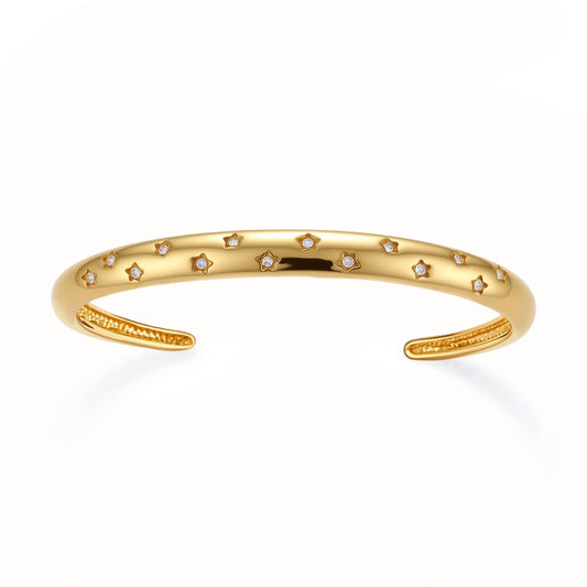 Polished 18K gold plated cuff bracelet with cubic zirconia set in star motifs on a cream background.