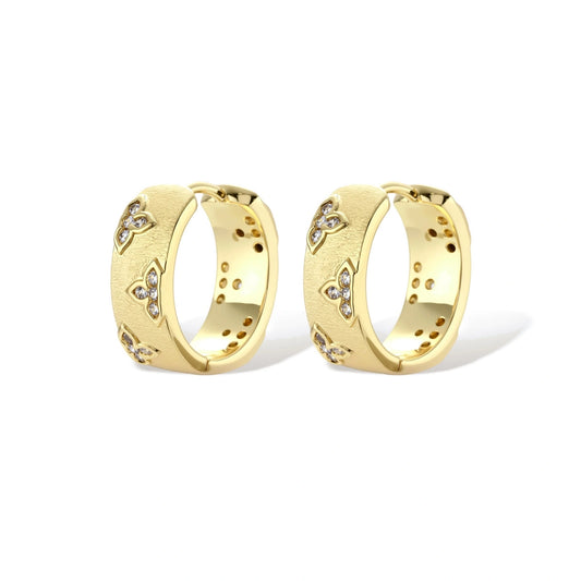 Gold-plated hoop earrings with textured surface and raised floral motifs set with clear zirconia stones on cream background.