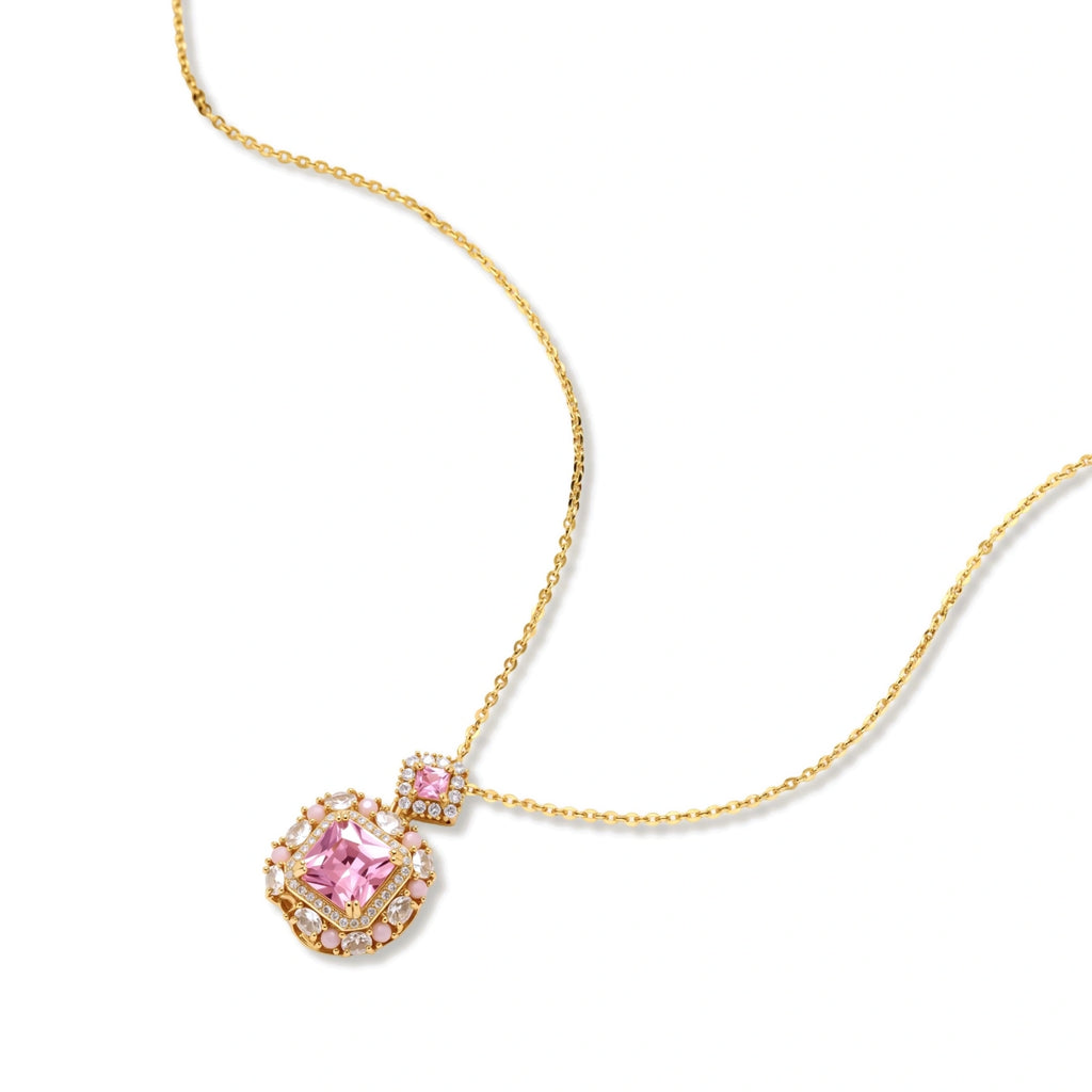 Ornate gold-plated jewelry set with rose pink zirconia center stones and crystal accents on cream background.