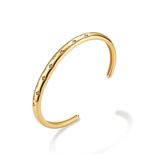 Polished 18K gold plated cuff bracelet with cubic zirconia set in star motifs on a cream background.